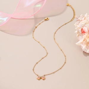 Close-up of golden beaded chain and pink enamel bow pendant with sparkling rhinestones