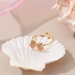 Detailed macro view of an adjustable gold-plated ring with a pink crystal bow design