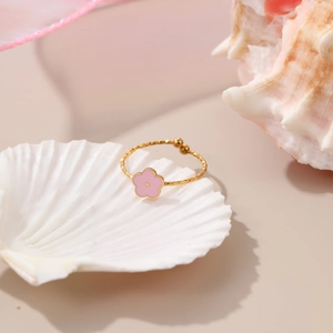 Close-up of golden rope-textured ring featuring a pink flower set on a white shell