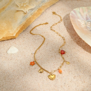 Detail of a gold stainless steel sea-themed necklace with shell and heart charms on sand