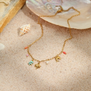 Close-up of golden ocean-themed necklace with starfish and palm pendants on beach sand