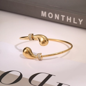 Gold-plated open bangle with teardrop ends and sparkling accents on gray background