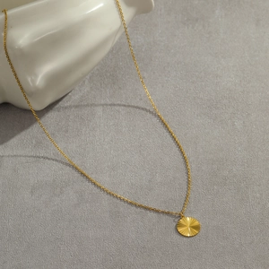 Detailed close-up of a golden sunburst engraved round pendant on a fine link chain necklace