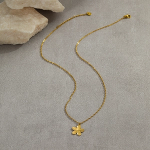 Macro detail of gold flower pendant necklace with radial texture on a stone background