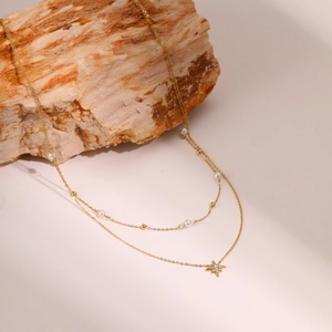 Detalle de collar dorado de doble capa con dije de estrella, perlas y cuentas de oro