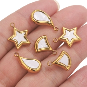 Detalle de colgantes de estrella y concha de acero dorado sujetos en la mano