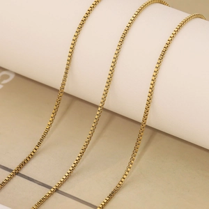 Close-up of golden box chain necklace with polished finish on a white jewelry stand
