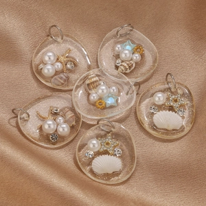 Transparent ocean resin pendants with pearls, seashells, and starfish on gold satin background