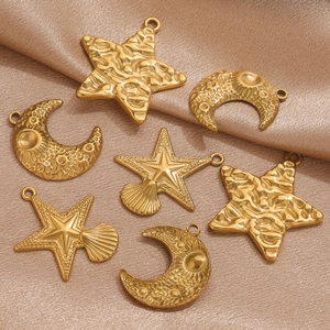 Macro detail of gold stainless steel moon and star pendants on champagne satin silk fabric
