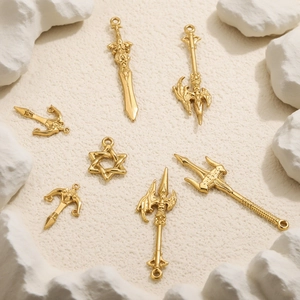 Golden DIY weapon pendants featuring sword and axe designs on a textured sand background