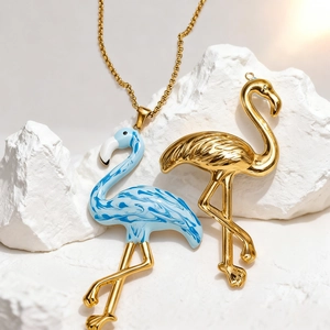 Enameled flamingo pendant and polished gold charm on a textured white rock background
