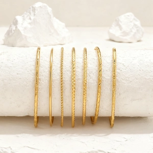 Set de 7 brazaletes apilables en tono dorado de acero con varios diseños texturizados
