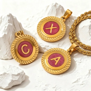 Collier chaîne torsadée dorée avec pendentifs ronds émaillés rose lettres A, C et X sur pierre