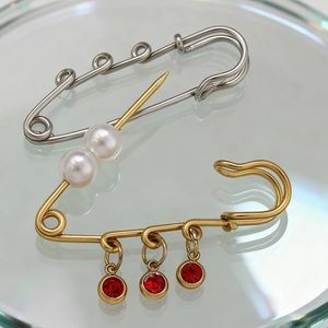 Vintage gouden roestvrijstalen speld met parels en rode edelsteenhangers op glas