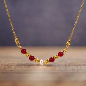 Golden stainless steel necklace with dark red beads and a central white pearl on wood