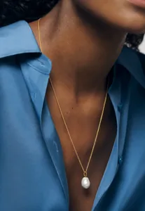 Close-up of a natural baroque pearl pendant on a gold necklace worn by a model