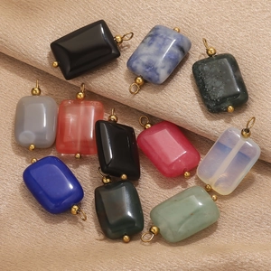 Vista de colgantes cuadrados de piedra natural con anillos dorados sobre tela de seda