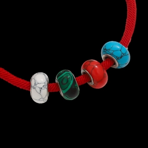 Detalle de pulsera de cuerda trenzada roja con cuentas de resina de colores y texturas