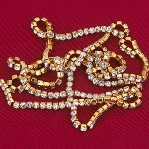 Vergulde klauwketting met transparante rhinestones op een rode getextureerde stof