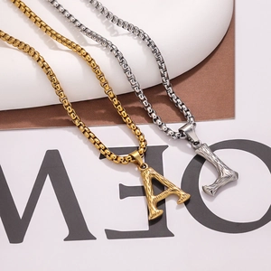 Macro detail of textured stainless steel box chain necklace with golden and silver letter charms