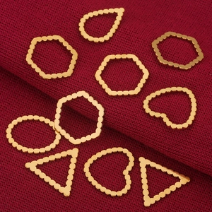 Detalle de varios dijes geométricos dorados con textura de cuentas en tela roja