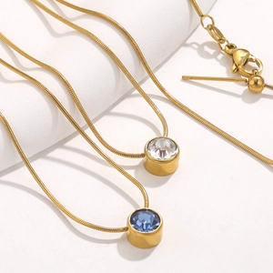 Gros plan sur colliers chaîne serpent dorée avec pendentifs en cristal blanc et bleu foncé