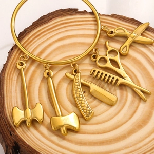 Detailed view of gold plated tool charms featuring axe, razor, comb and scissors on wood