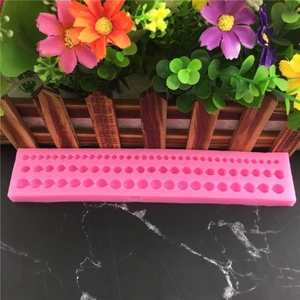 Stampo in silicone rosa per perle con tre file di cavità su sfondo di marmo nero