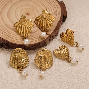 Golden twisted heart and round earrings with white pearl pendants on wooden base