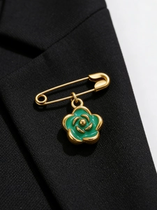 Detailed close-up of a green camellia flower pendant on a golden brooch pin over dark fabric