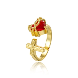 Bague ouverte dorée avec zircon cœur rouge et symbole croix sur fond blanc épuré