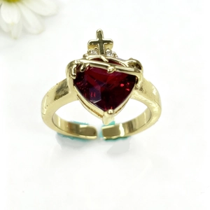 Gros plan d'une bague dorée ajustable avec cœur en zircon rouge et détail croix gothique