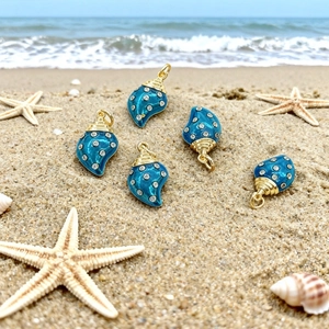 Macro di ciondoli a conchiglia placcati in oro 18k con smalto blu sulla spiaggia