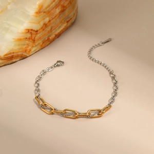 Detalle de joyería de cadena en dos tonos oro y plata sobre fondo de piedra natural
