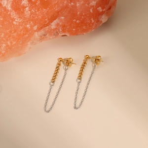 Close-up of gold and silver mixed chain tassel earrings on decorative warm stone background