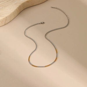 Close-up of gold and silver two-tone stainless steel curb chain necklace on stone