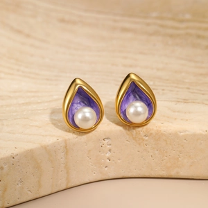 Detail shot of teardrop gold earrings with purple enamel texture and white pearl inlay