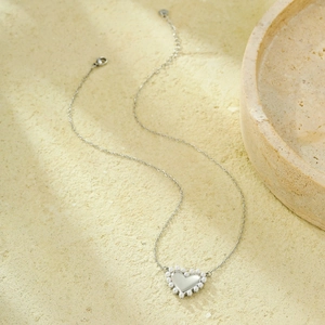 Primer plano de collar con colgante de corazón y perlas en fondo de piedra natural