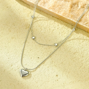 Detalle de collar de capas plateado con colgante de corazón y cadena de serpiente
