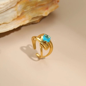 Detail of 18K gold-plated irregular ring with a square blue zircon on a beige surface
