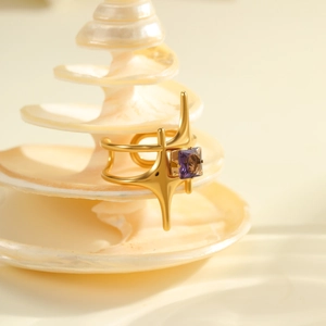 Detail of starburst gold ring with purple zircon stone on a white spiral shell base