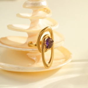 Macro detail of irregular gold ring with purple zircon stone on a white conch shell
