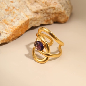 Detailed macro view of an irregular gold-plated ring with purple zircon on natural stone