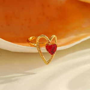 Détail d'une bague cœur ajourée avec zircon rouge posée sur un coquillage naturel