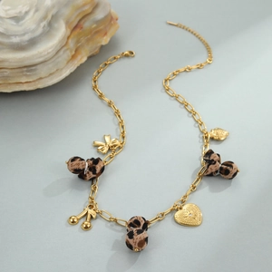 Detail van luipaardprint bedeltjes en een gouden hart hanger aan een roestvrijstalen ketting