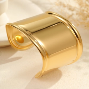 Brazalete ancho abierto de acero inoxidable dorado pulido sobre un fondo de piedra liso