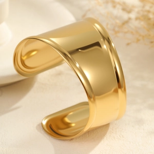 Primer plano del brazalete ancho dorado de acero inoxidable pulido sobre piedra