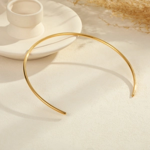 Minimalist gold titanium steel torque necklace with a polished mirror finish on white background
