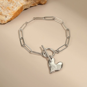 Detail van een zilveren hartvormige hanger aan een paperclip-armband met OT-sluiting