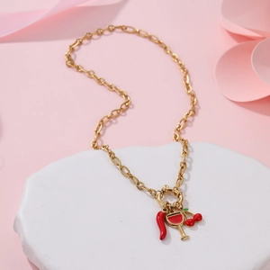 Goldkette mit Kirsch- und Chili-Anhängern auf einem weißen strukturierten Steinsockel
